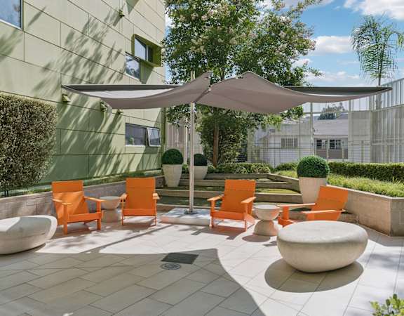 A patio with orange chairs and a white umbrella.