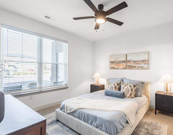 A bedroom with a bed, two lamps, and a painting on the wall.