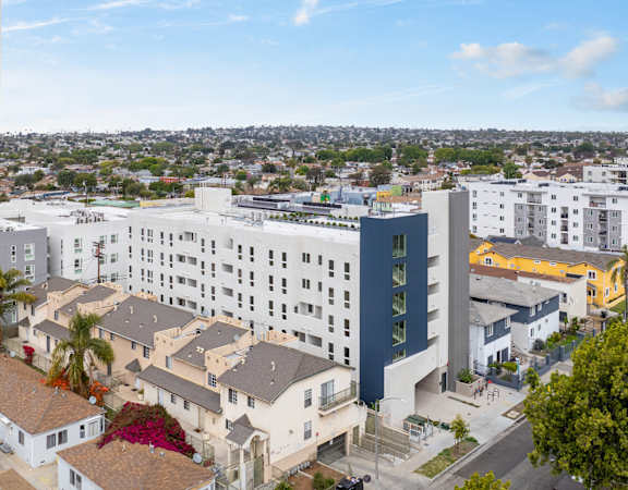 A modern building with a blue accent wall is surrounded by other buildings and houses.