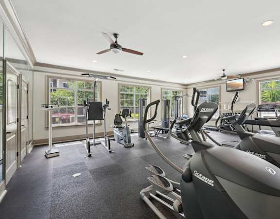 A gym with a row of treadmilers and elliptical machines.