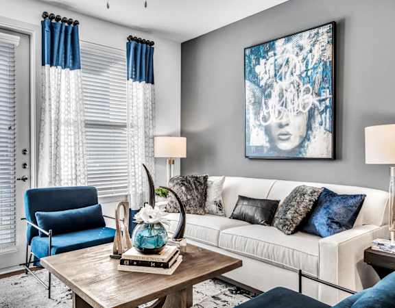 A living room with a white couch, blue chair, and a painting on the wall.