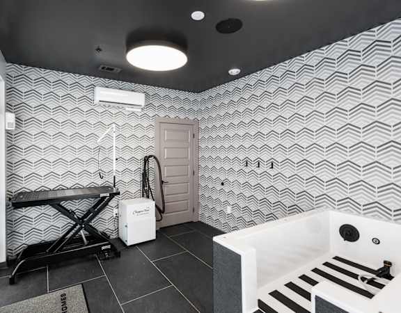A bathroom with a white tub and a black and white tiled wall.