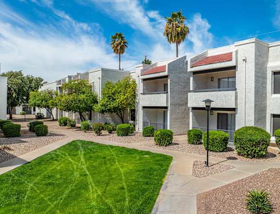 a white apartment building with a green lawn and palm trees at Tides on Southern, Mesa, AZ 85204