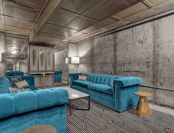 A blue couch is in the middle of a room with concrete walls.
