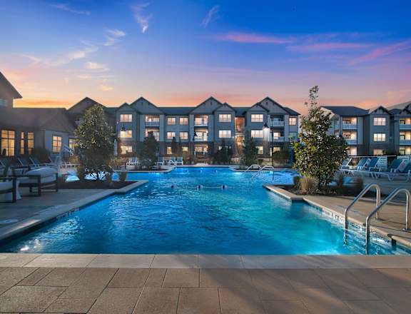 A swimming pool in front of apartment buildings at dusk.
