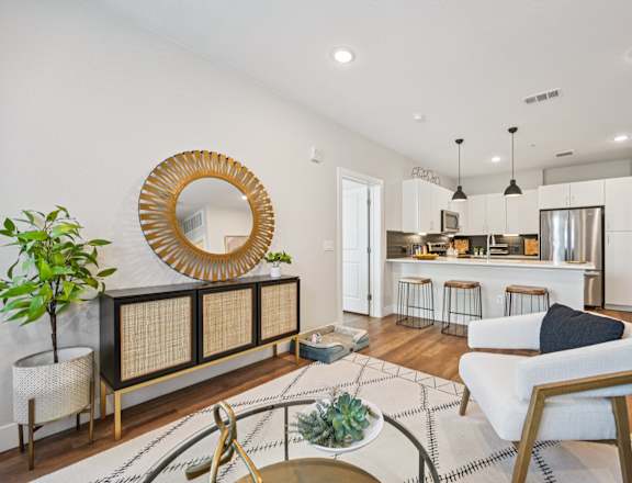 A living room with a white couch, a round mirror, and a wooden coffee table.