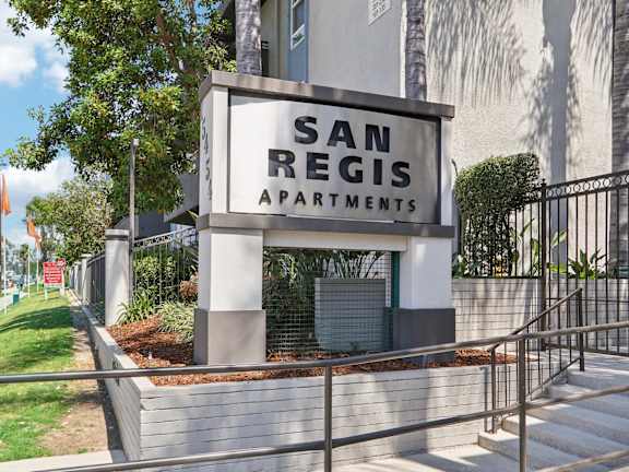 A sign for San Regis Apartments is displayed in front of a building.
