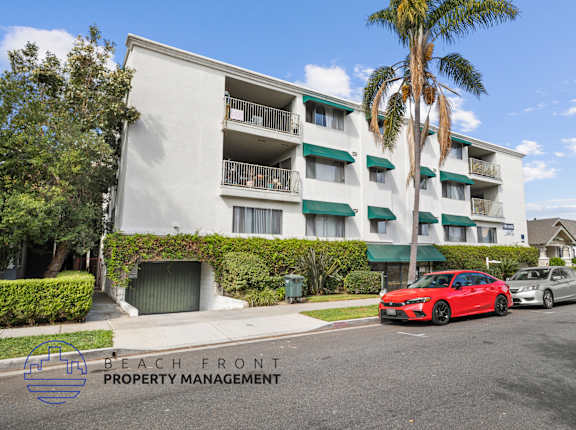 A red car is parked on the street in front of a white apartment building.