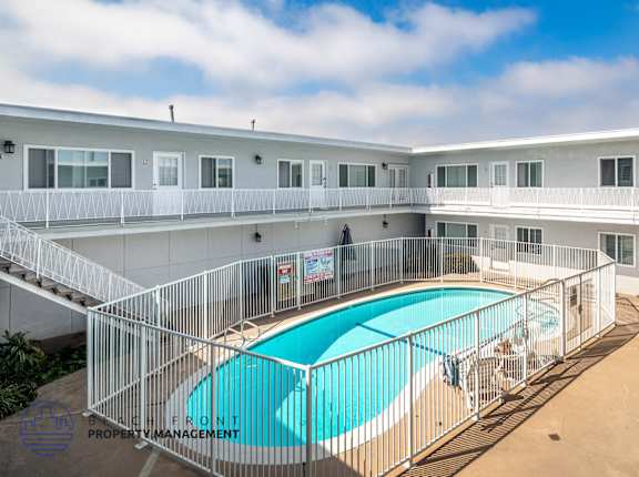 A pool surrounded by a fence in a sunny courtyard.