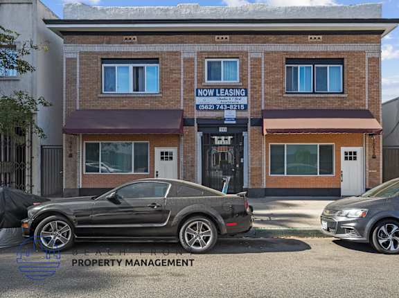 the front of the now leasing building with two cars parked in front