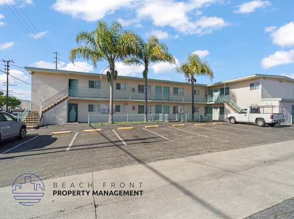 A parking lot with a building and palm trees in the background.
