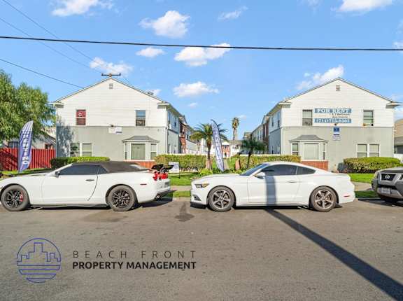 Three white cars are parked in front of a building with a sign that reads "Beach Front Property Management.".