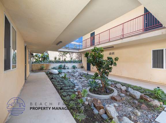 A balcony with a red railing overlooks a landscaped garden area.