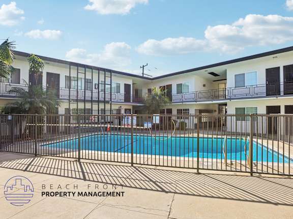 A pool surrounded by a fence and a building with balconies.