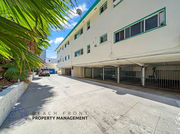 A white building with green trim and a sign that says "Beach Front Property Management".