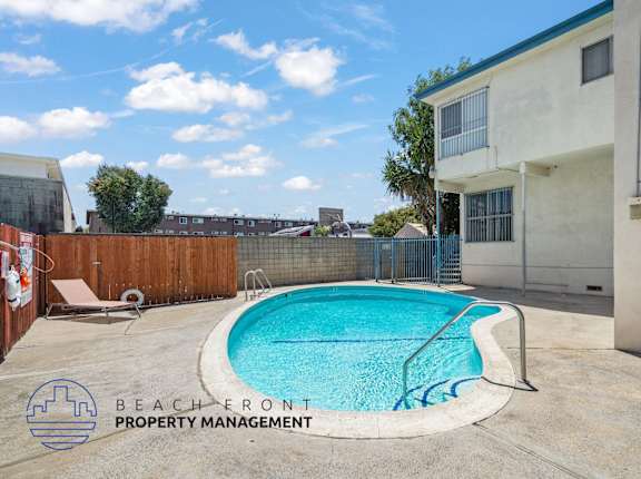 A pool in a backyard with a fence and a building in the background.