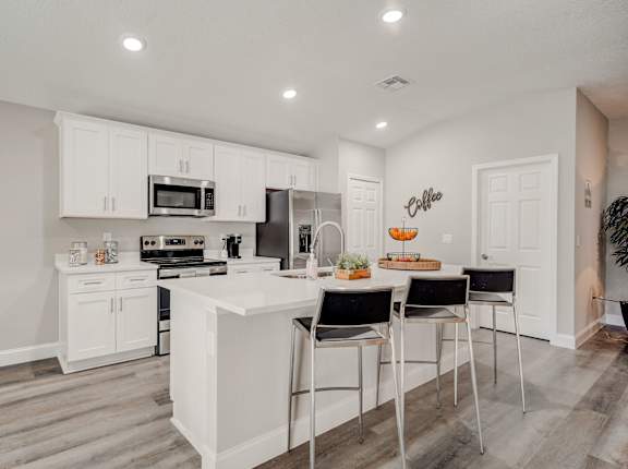 Open kitchen with a countertop, three stools, and modern appliances.
