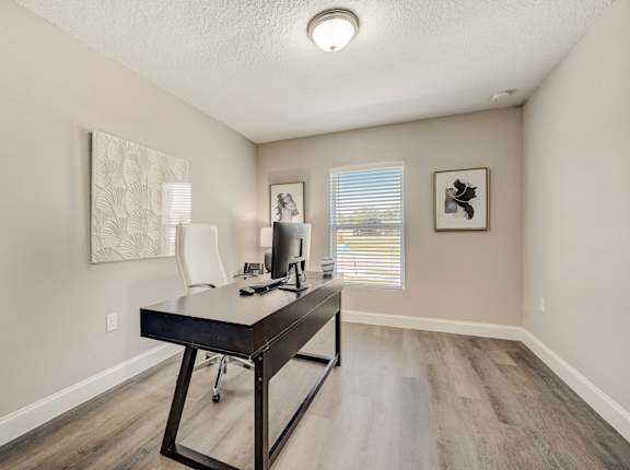 Office space with a desk, chair, computer, window, and paintings.