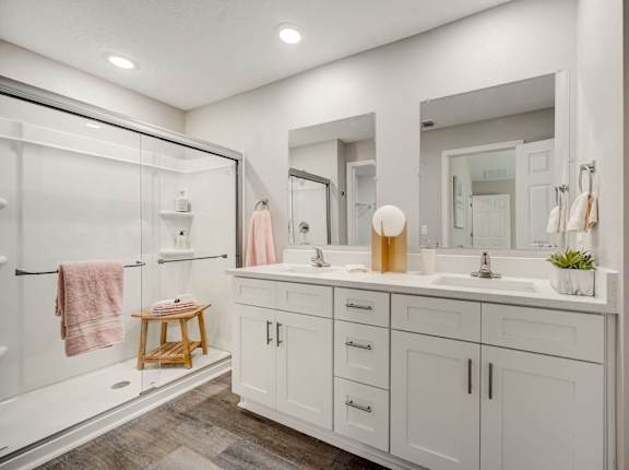 Spacious bathroom with shower enclosure, dual sinks, mirrors, and a cabinet.