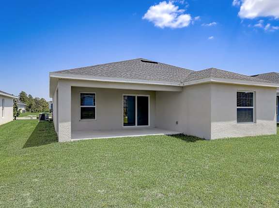 House with a grey roof, glass doors, yard, and blue sky.