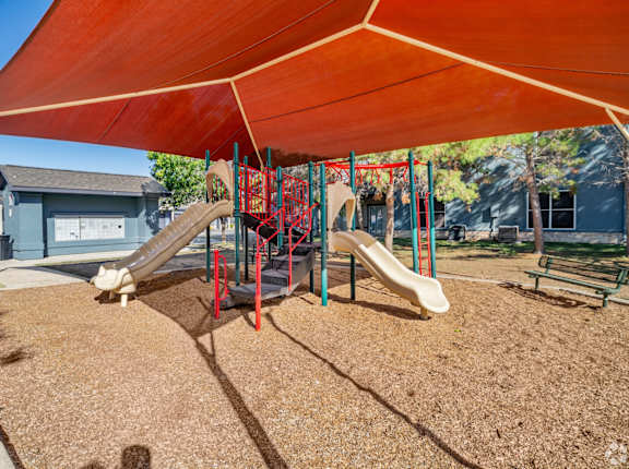A playground with a red canopy and a slide.
