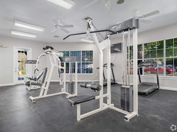 A spacious gym with a variety of equipment including a treadmill, a weight bench, and a barbell.