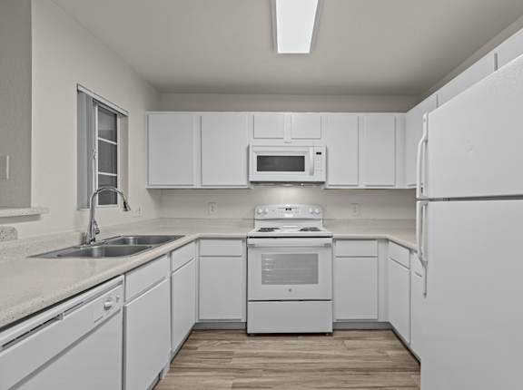 A white kitchen with a refrigerator, sink, and stove.