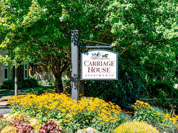A sign for Carriage House Apartments is surrounded by flowers.