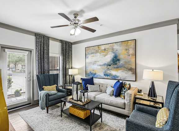 A living room with a grey couch, a black chair, a coffee table, and a painting on the wall.
