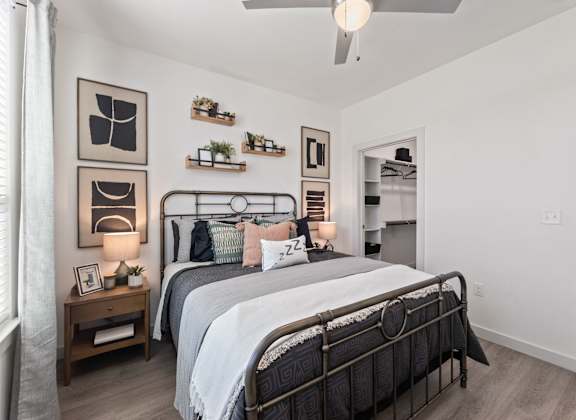 A bedroom with a large bed, a nightstand with a lamp, and a wall-mounted shelf with plants.
