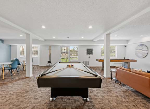A billiard table is in the middle of a room with chairs and a couch.