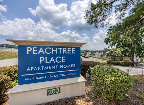 A sign for Peachtree Place Apartment Homes in front of a tree.
