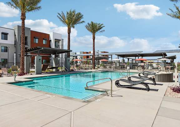 A pool surrounded by palm trees and lounge chairs at Ironwood Ranch Apartments,Maricopa,AZ