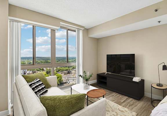 A living room with a couch, a chair, a coffee table, a television, and a window with a view of the city.