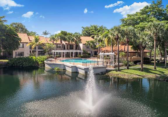 A fountain in the middle of a pond in front of a building.