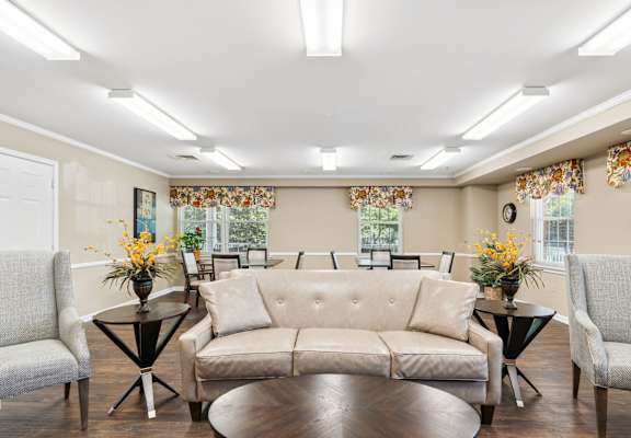 A living room with a beige sofa, two chairs, and two tables with vases of flowers.