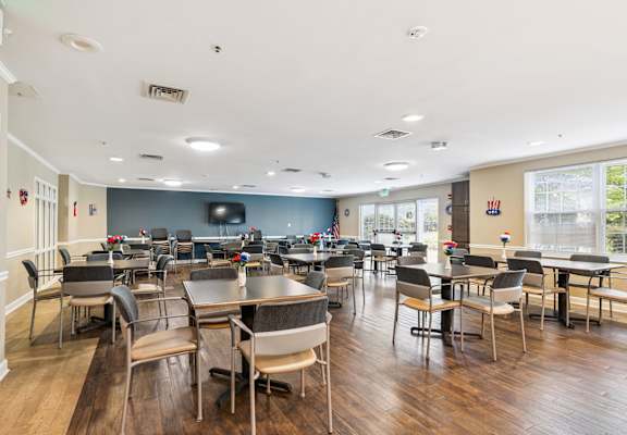 A large room with tables and chairs and a TV on the wall.