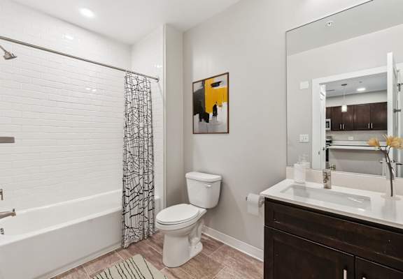 A bathroom with a white toilet, a shower with a black and white curtain, and a painting on the wall.
