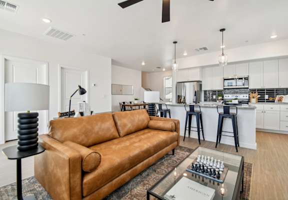 A living room with a tan couch and a chess board on the coffee table.