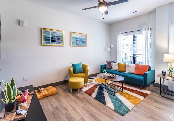 Butchertown Apartments - Martin on Main - Living Room with Colorful Area Rug, Couch, Chair, Coffee Table, Ceiling Fan, and Window.
