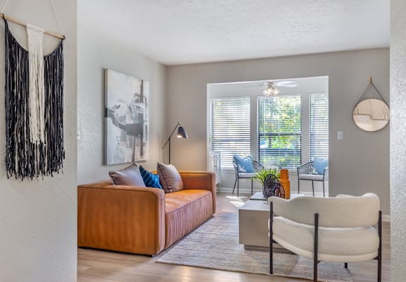 A living room with a brown couch, a white chair, and a hanging decoration on the wall.