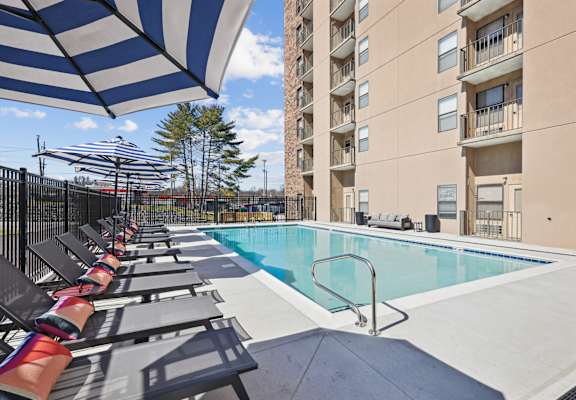 A pool area with sun loungers and a tall building in the background.