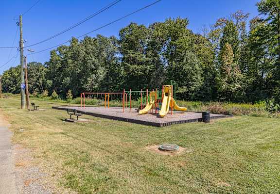 A playground with a yellow slide and a bench.