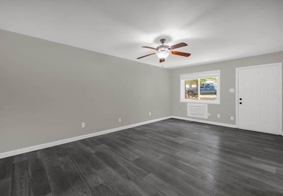A room with a ceiling fan and a window showing a parking lot.