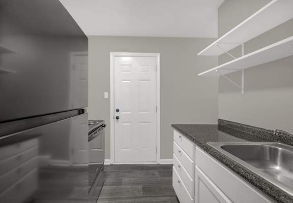 A kitchen with a black refrigerator, white door, and a granite countertop.
