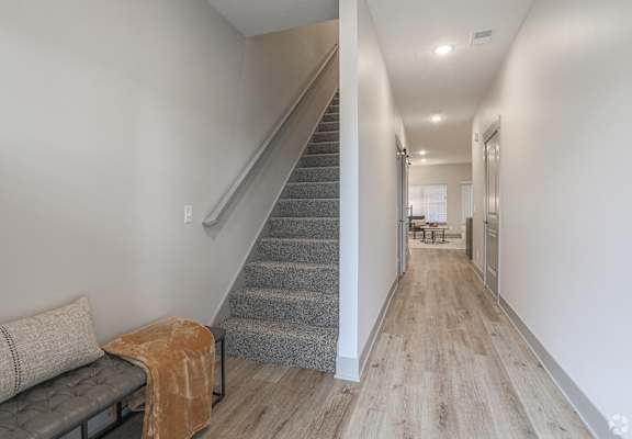 A long hallway with a staircase and a bench with a blanket on it.