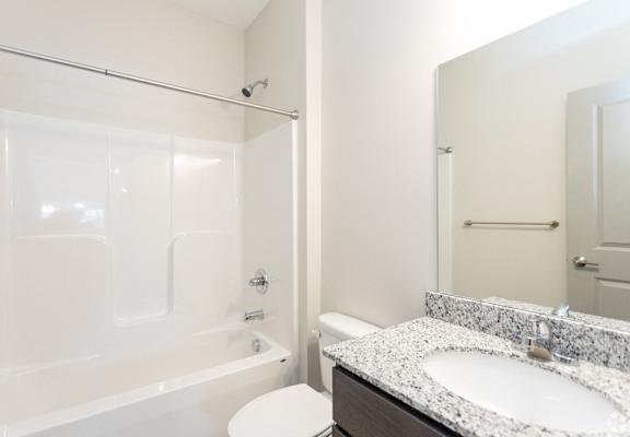 A white bathroom with a marble counter top and a walk in shower.