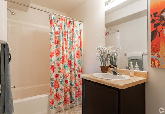A bathroom with a floral shower curtain and a brown vanity.