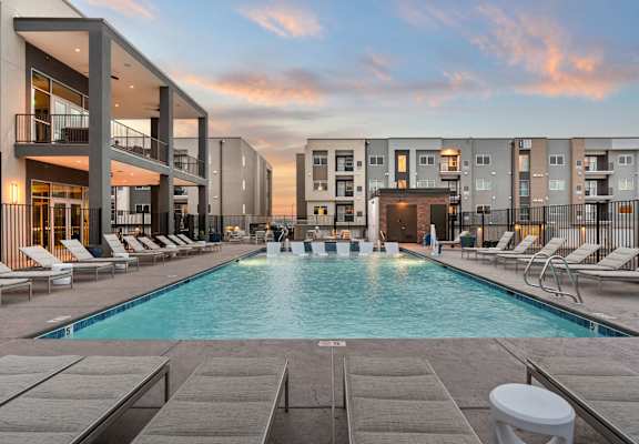 A swimming pool surrounded by lounge chairs and buildings.