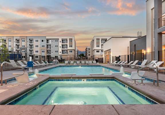A swimming pool surrounded by lounge chairs in front of apartment buildings.